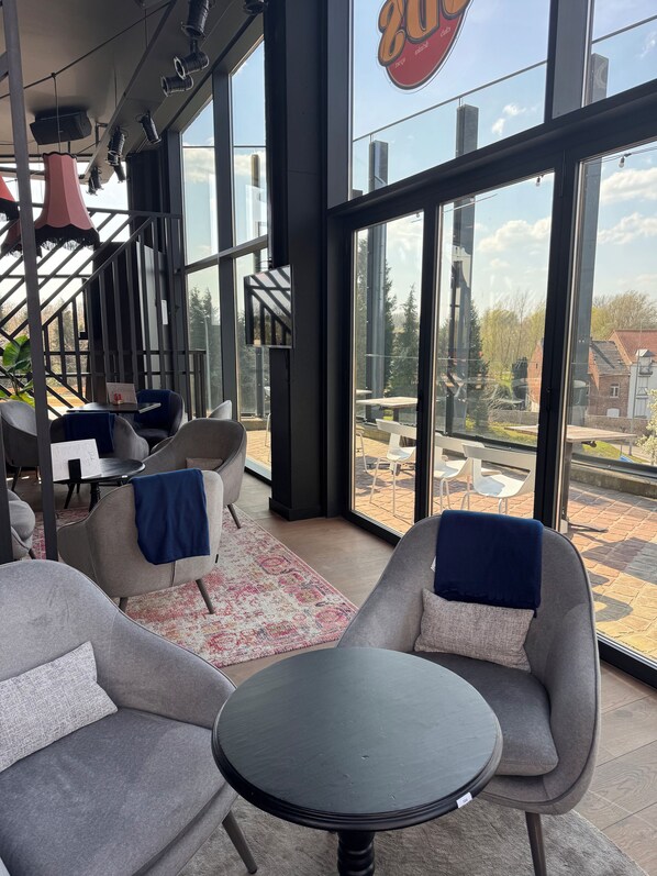 A modern interior with large windows, grey upholstered chairs, a round table, and a visible outdoor view.