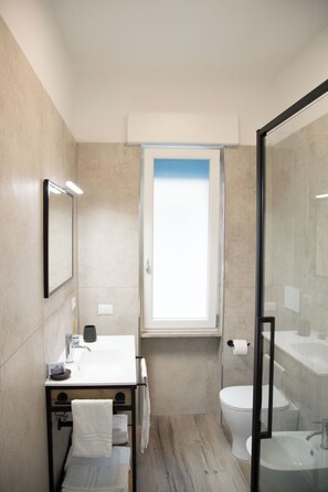 Un baño moderno con un espejo grande, un lavamanos, un inodoro y una ducha con paredes de cristal.