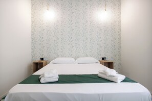A neatly made bed with white linens, two bedside tables with lamps, and a floral wallpaper pattern. - Charming 2-bedroom apartment in delightful Napoli with WiFi, AC (Napoli)