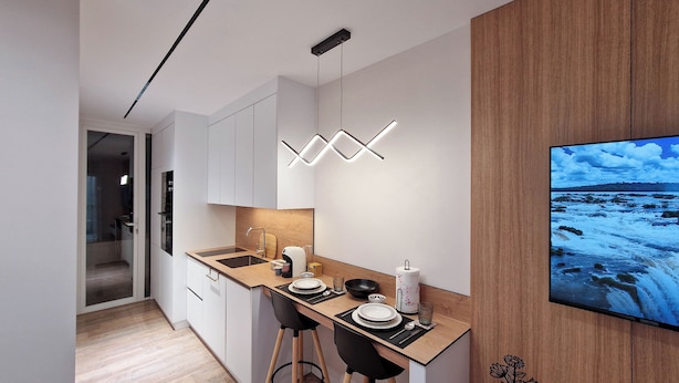A modern kitchen with a wooden countertop, white cabinets, and a built-in TV displaying a scenic view. - Beachfront Luxury Studio (Durrës)