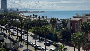 A coastal cityscape with a busy street lined with palm trees, a beach, and a large building in the background. - Beachfront Luxury Studio (Durrës)