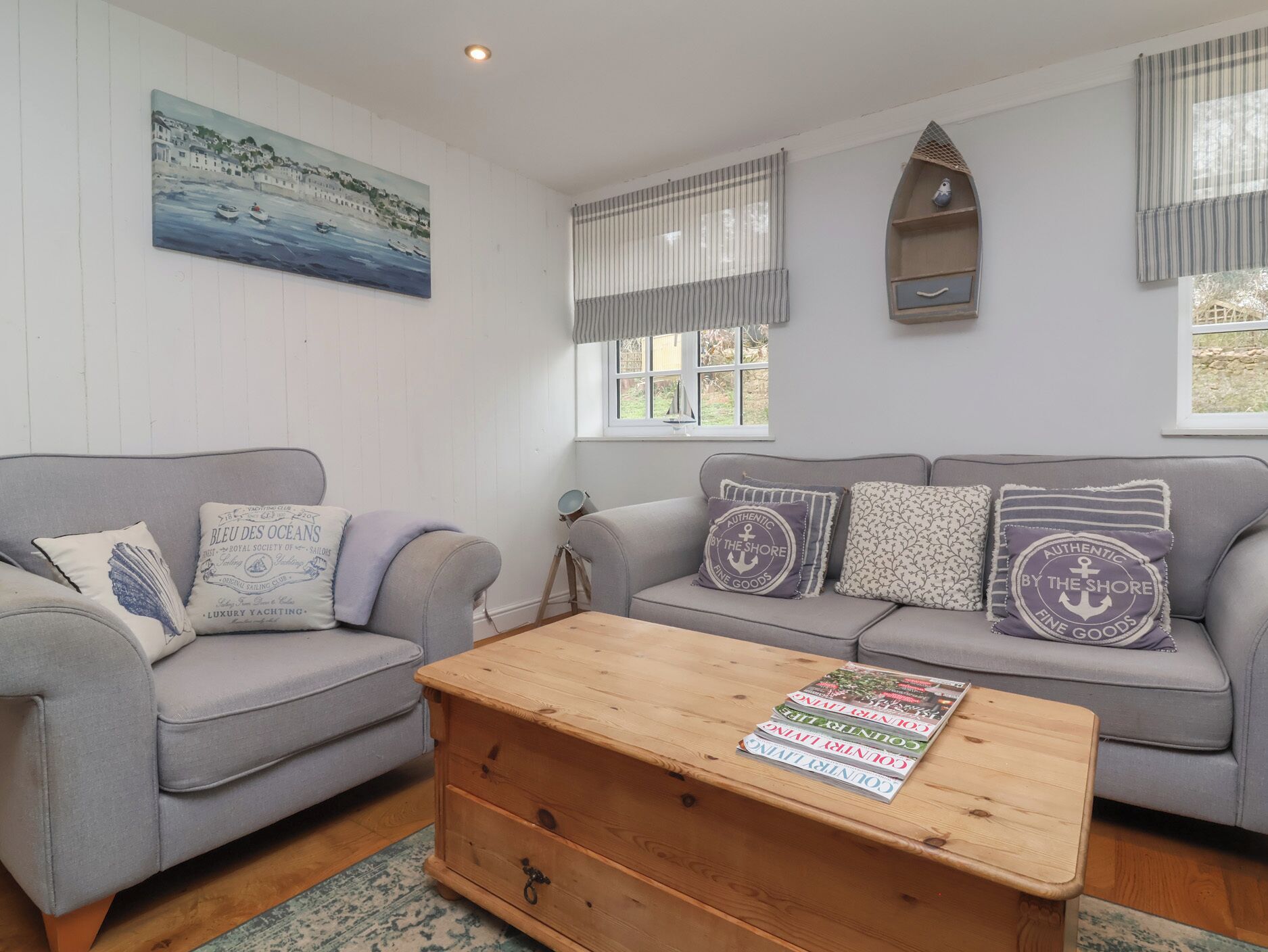 A cozy living room with two grey sofas, a wooden coffee table, and a painting of a coastal scene.