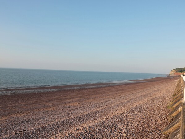 A pebble beach with a clear sky and distant cliffs. - Gatekeeper's Cottage (Minehead)