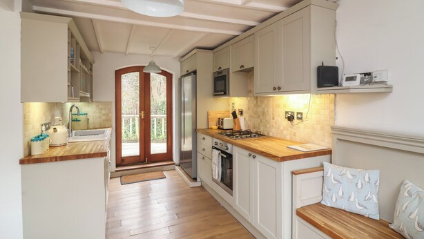 Una cucina con pavimento in legno, mobili bianchi, forno a incasso, microonde e piano cottura.