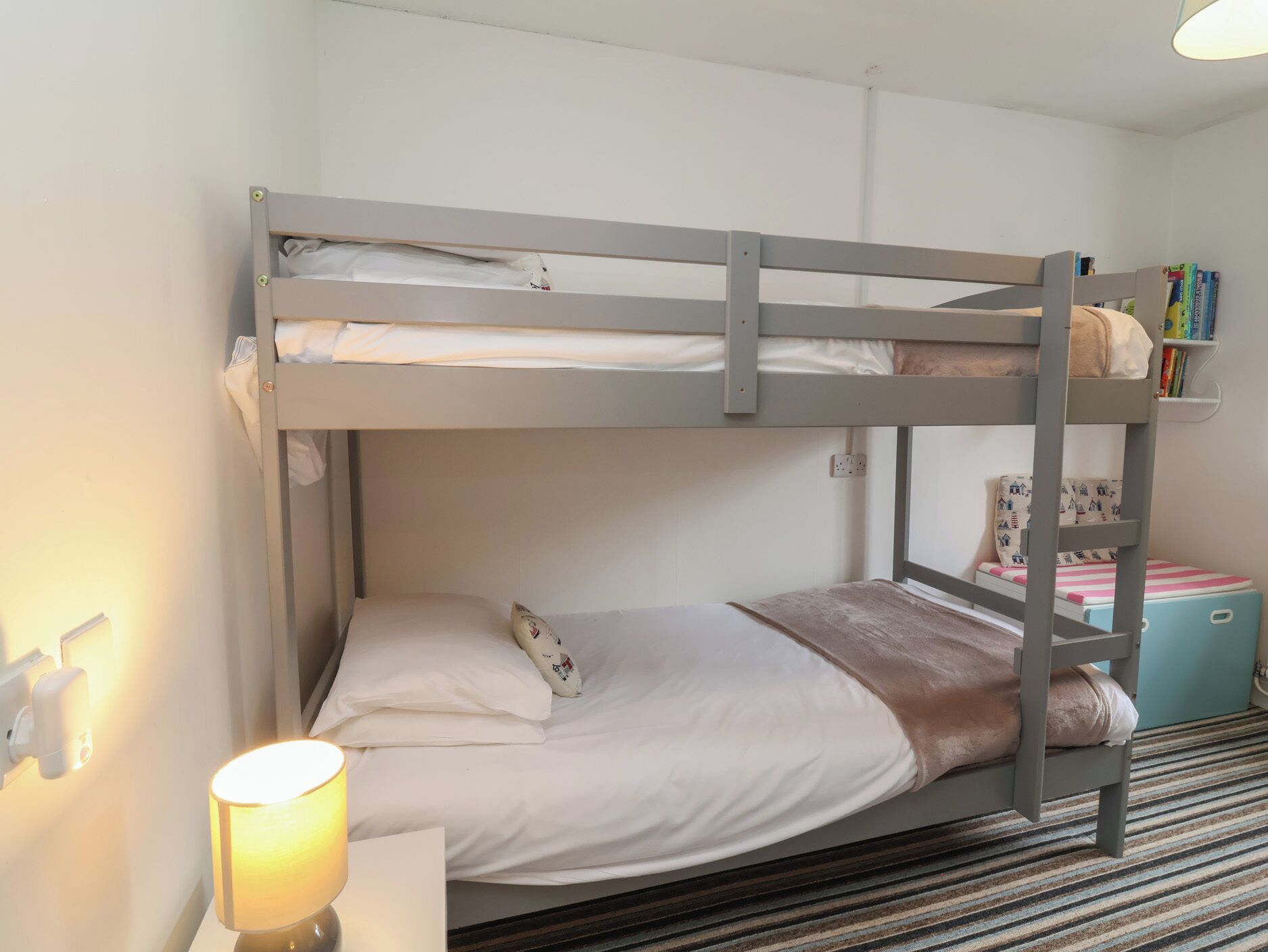 Dormitorio con literas, mesita de noche, lámpara y estantería.