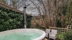 Una vasca idromassaggio in giardino con un decking in legno e poltrone in vimini.