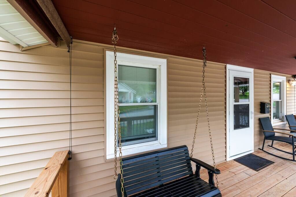 A porch with a black bench, a wooden bench on the left, and a door with a window.