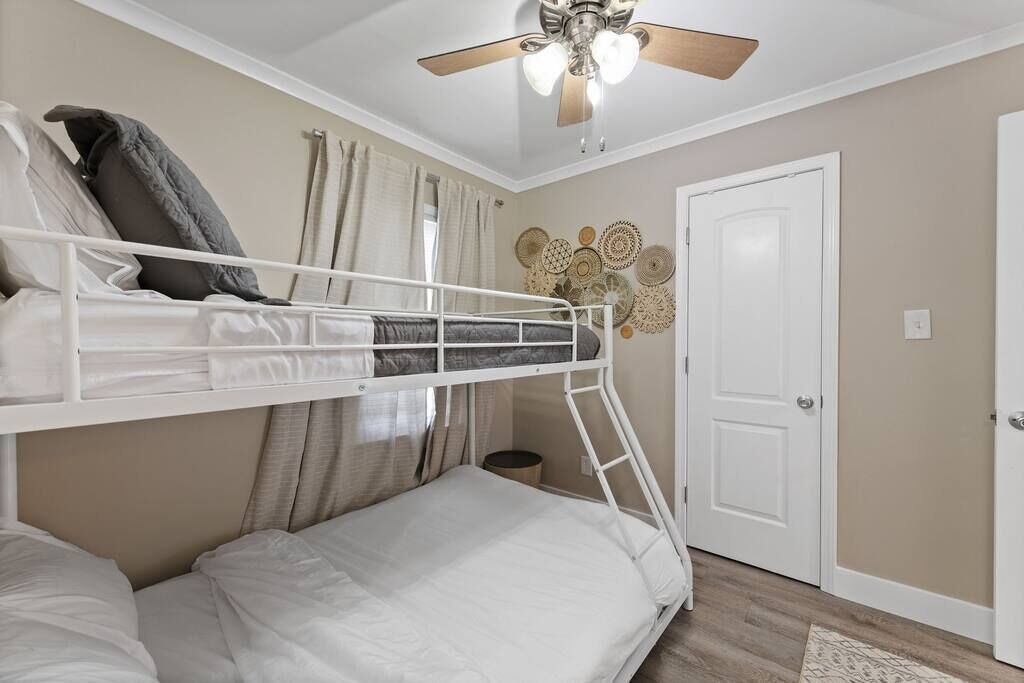 A bunk bed room with a ceiling fan, a door, and decorative wall art.
