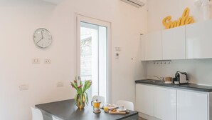 Una cocina moderna con armarios blancos, cafetera y tostadora. Hay una mesa de comedor con sillas y un florero con flores.