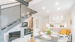 Una cocina moderna con horno empotrado, un comedor con mesa lista para cuatro comensales y una escalera con barandilla de metal.