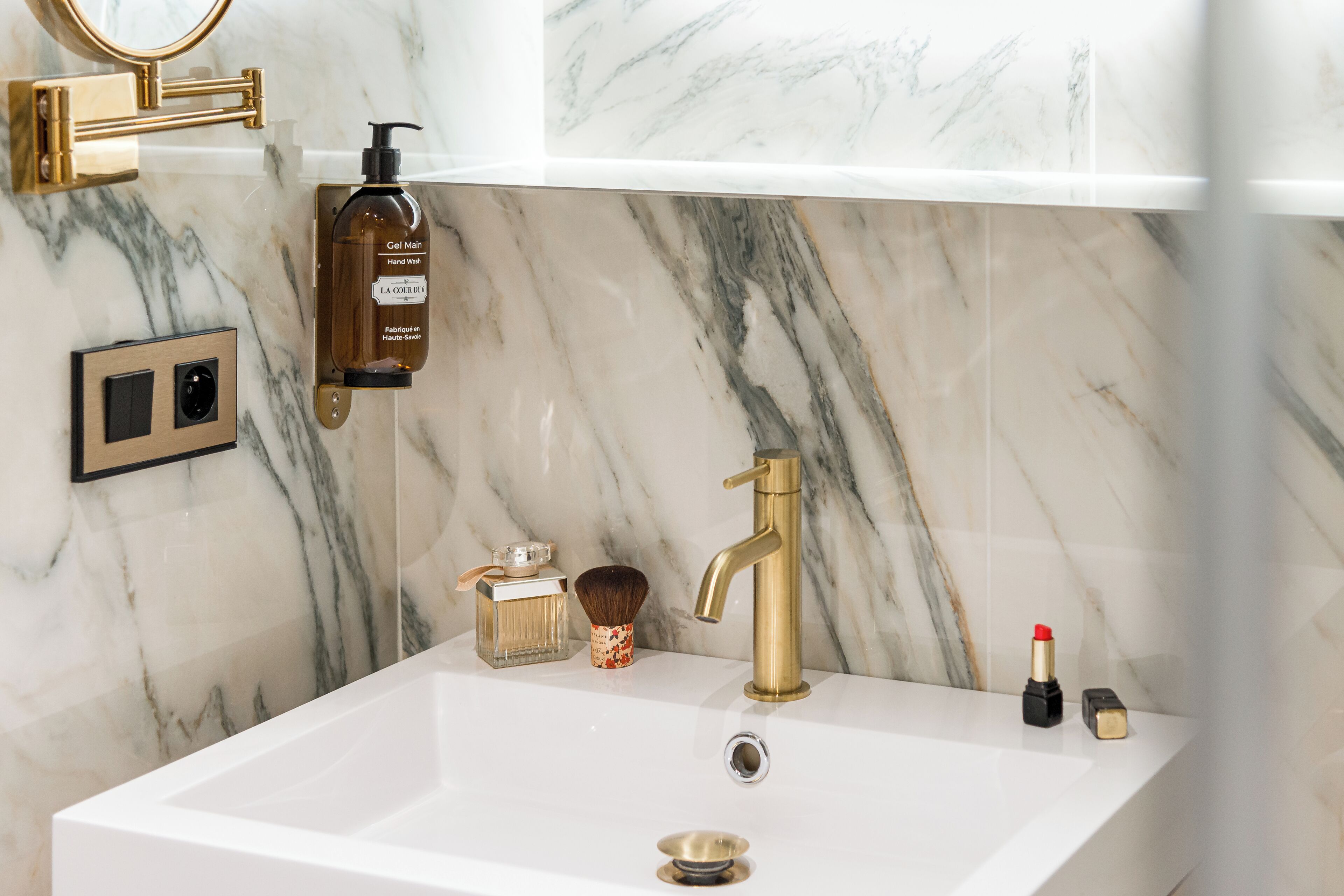 A bathroom with a marble sink, gold faucet, and toiletries.