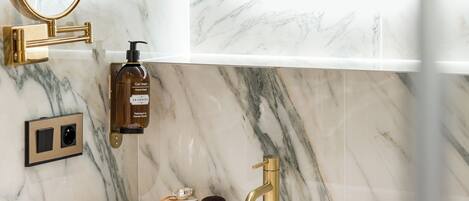 A bathroom with a marble sink, gold faucet, and toiletries.