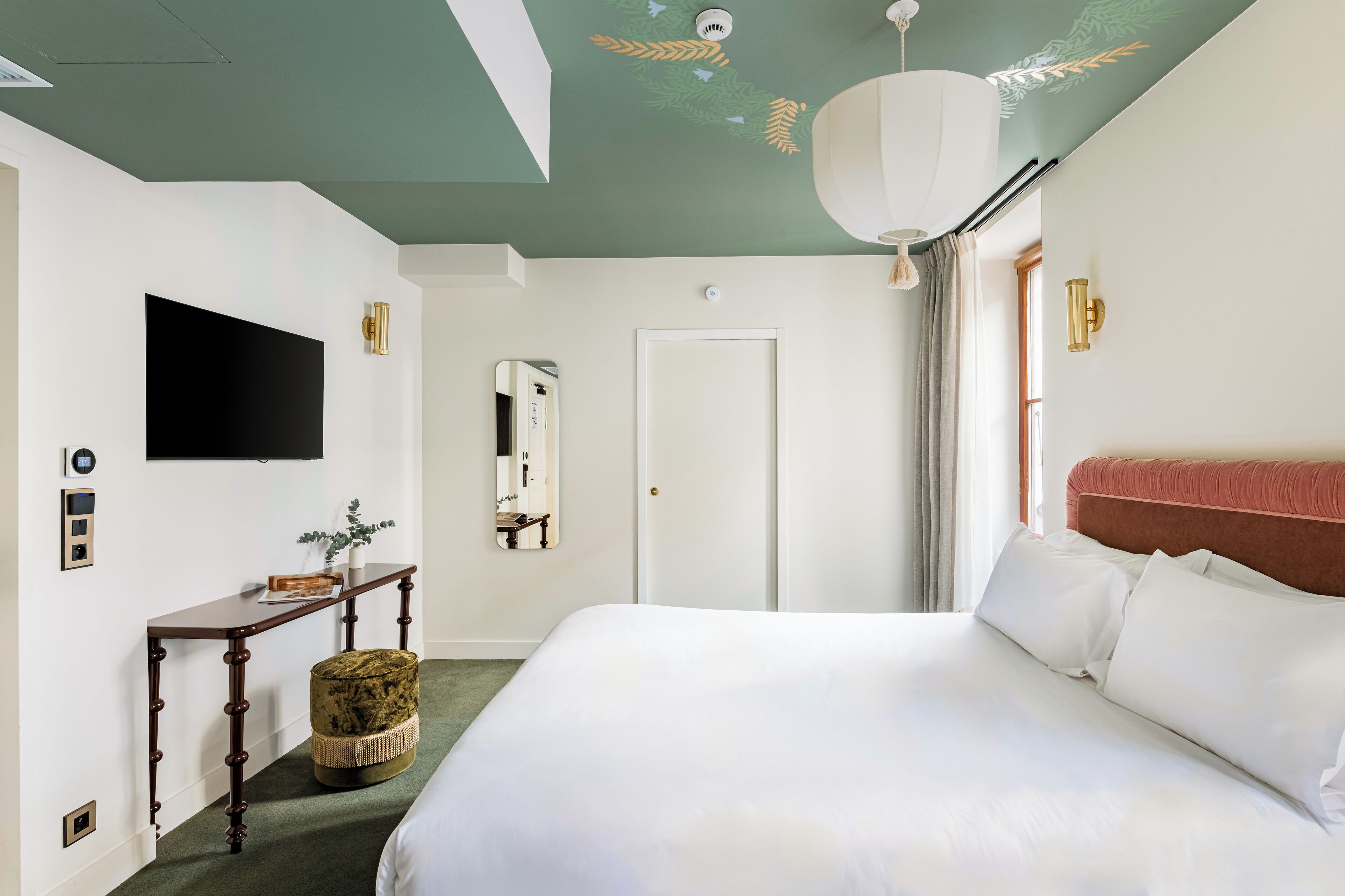 Un dormitorio con una cama grande, una consola de madera, un espejo y un televisor en la pared.