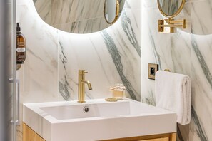 A bathroom with a white sink, gold faucet, and marble walls. - La Cour du 6 (Annecy)