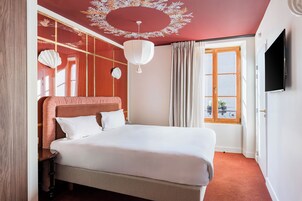Hotellihuone, jossa on suuri sänky, kattotuuletin, televisio ja ikkuna, jossa on verhot.