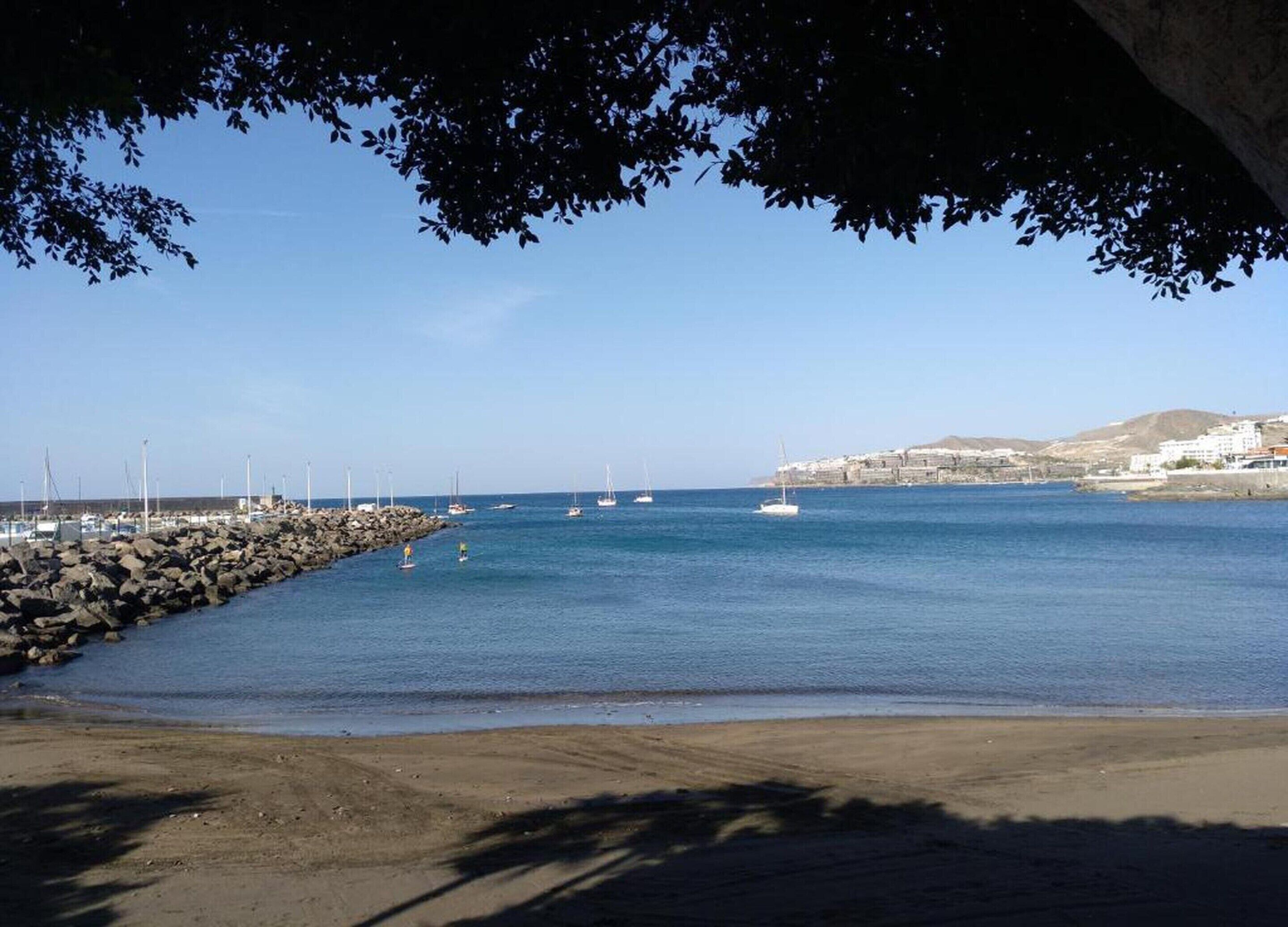 A coastal scene with a rocky breakwater, calm sea, and sailboats.