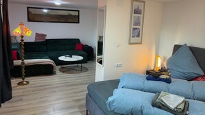 Ein Wohnzimmer mit einem grünen Sofa, einem runden Couchtisch und einer Lampe. An der Wand hängt ein gerahmtes Bild und es befindet sich ein Spiegel im Raum.