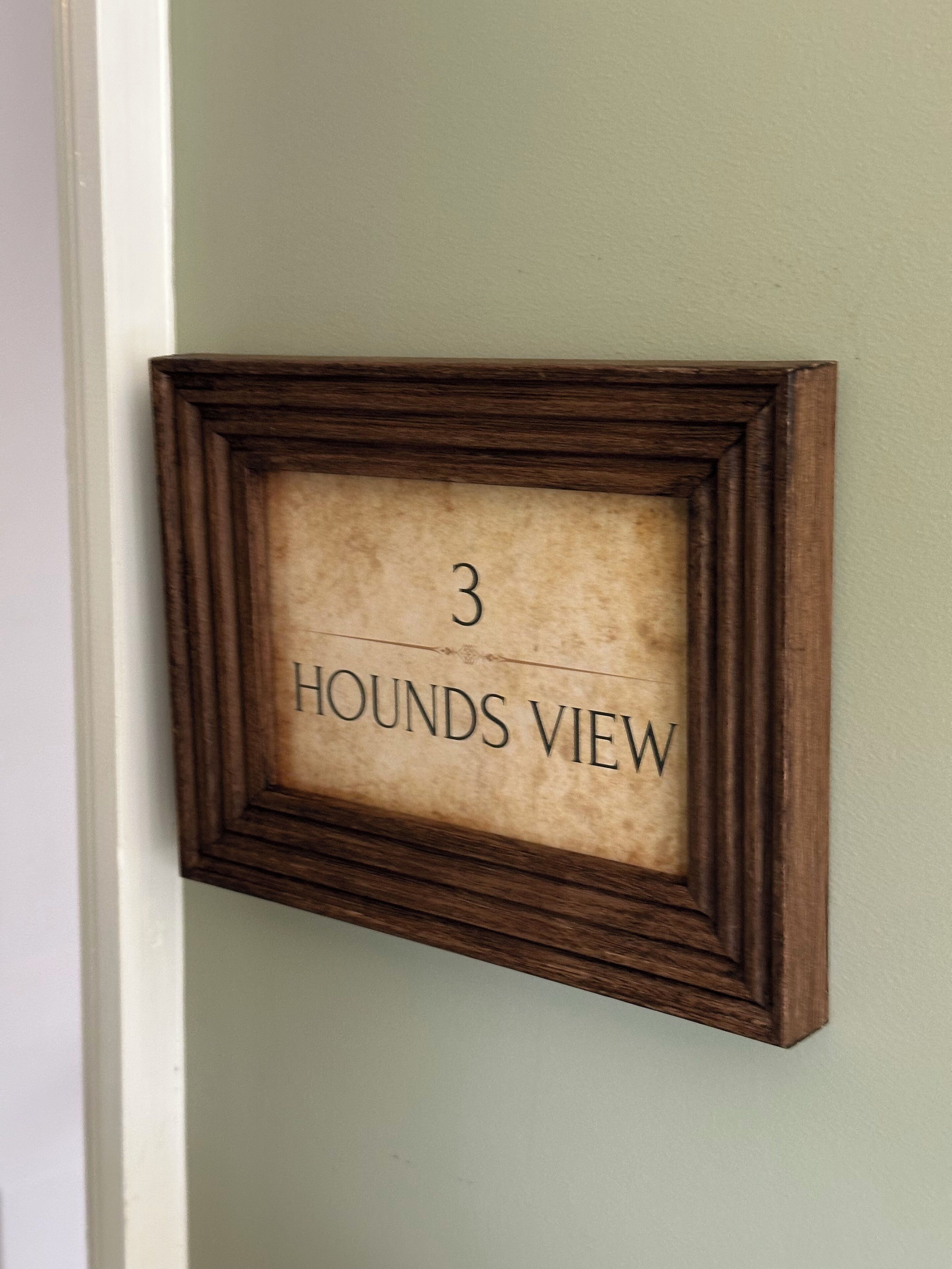 A framed sign with the text "3 HOUNDS VIEW" on a wall.
