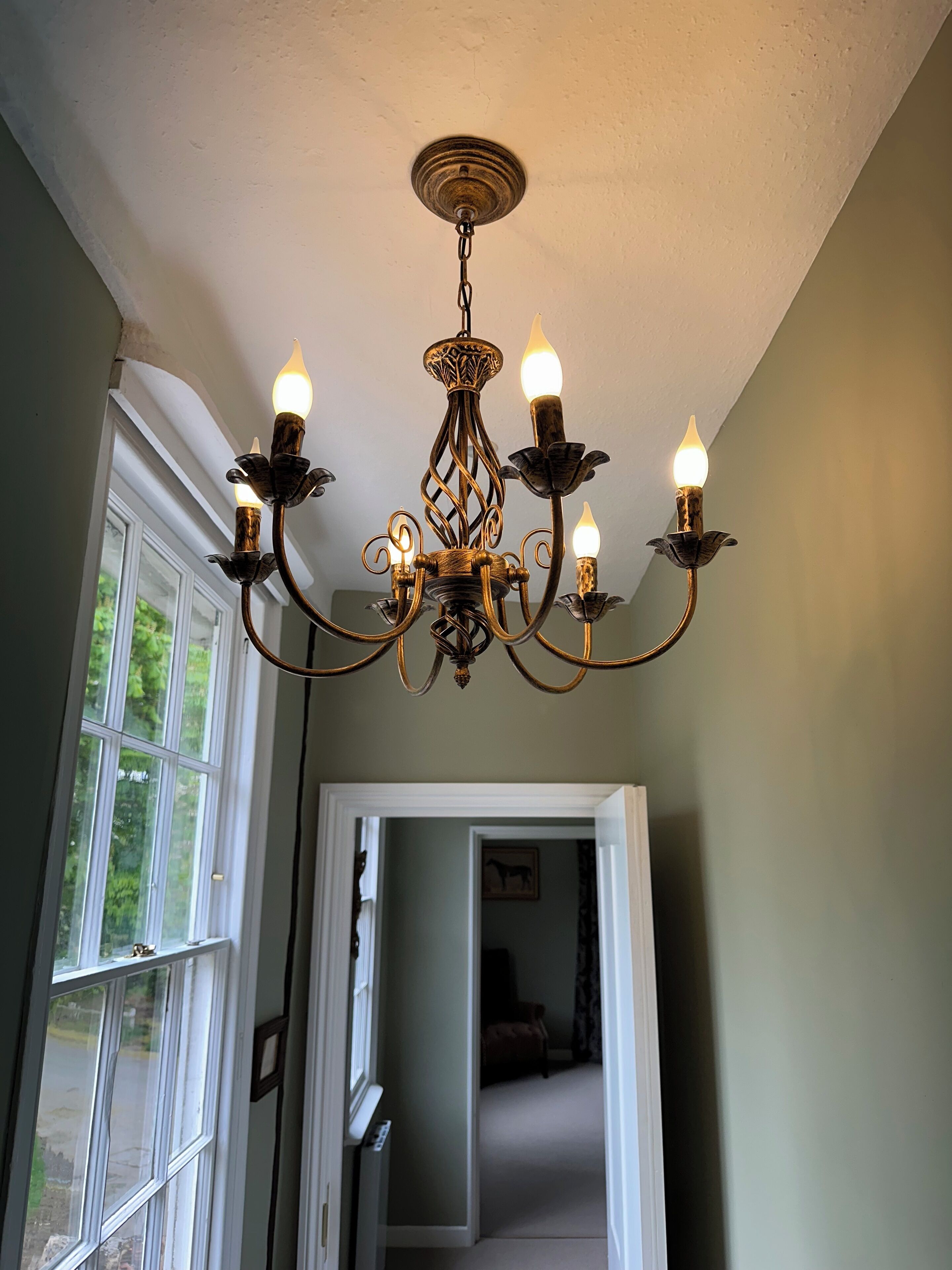 Um candelabro com várias luzes semelhantes a velas, uma porta branca e uma janela com vista para vegetação.