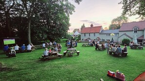 Un espacio al aire libre para reuniones con mesas de picnic y una pantalla de televisión.