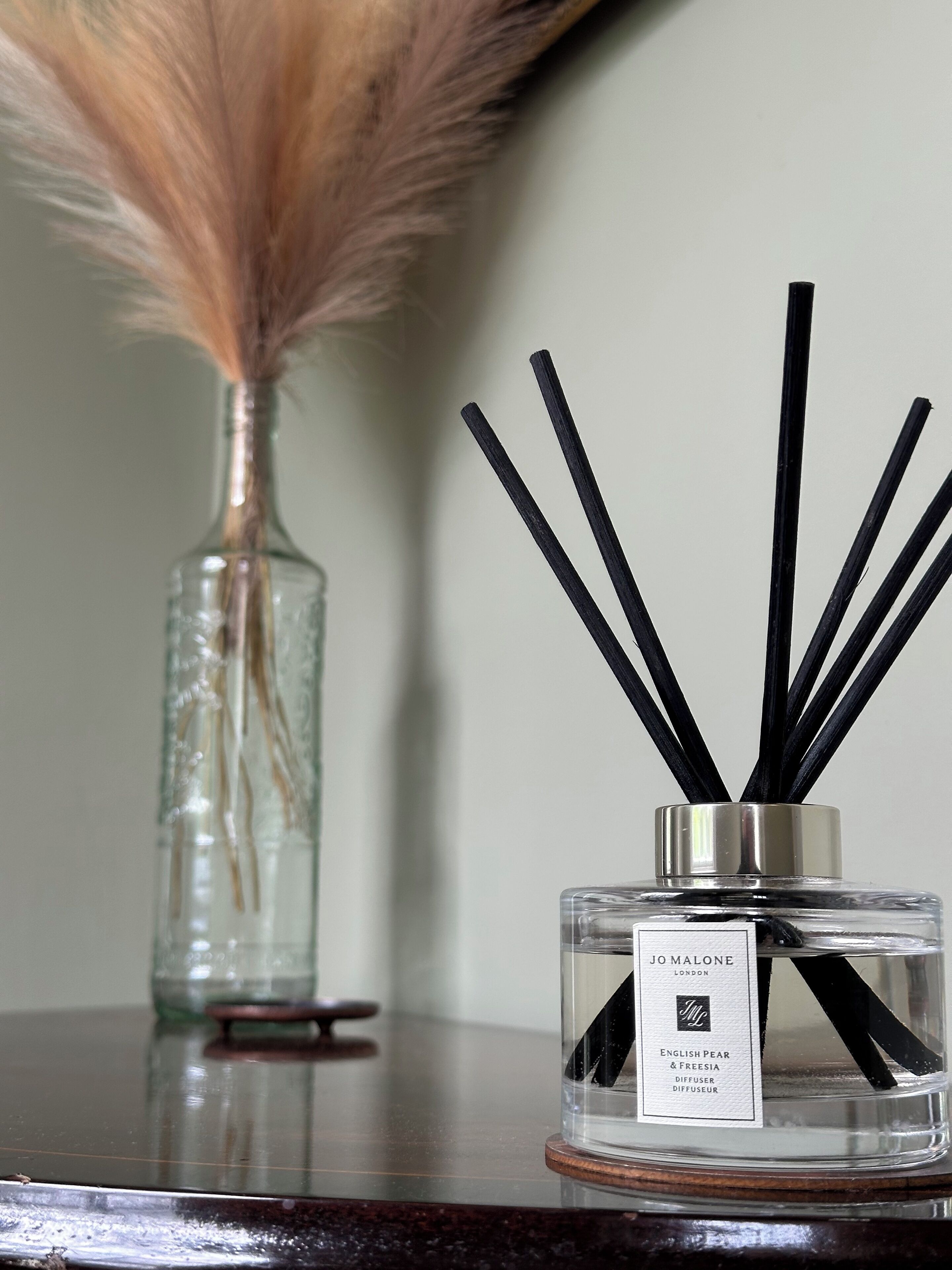 A clear glass diffuser with black reeds and a label indicating it is from Jo Malone London.