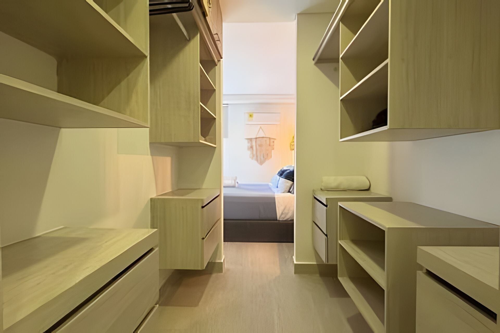 Vestidor estrecho con múltiples estantes y cajones, que conduce a una zona con cama.