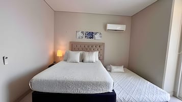 Un dormitorio con cama, mesitas de noche, aire acondicionado de pared y ventana.