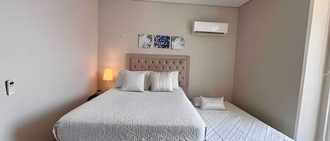 Un dormitorio con cama, mesitas de noche, aire acondicionado de pared y ventana.