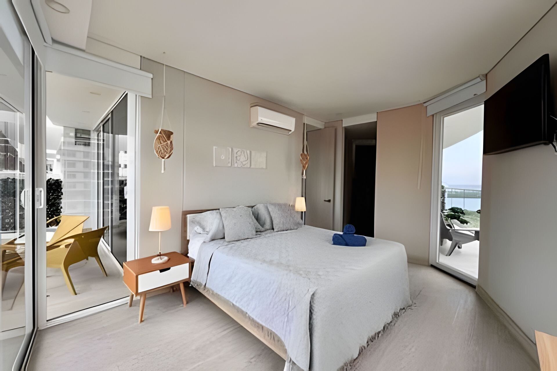 A modern bedroom with a bed, bedside table, lamp, and a view of the outdoors.