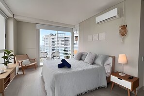 A modern hotel room with a large bed, a desk, a chair, and a view of high-rise buildings. - Edificio Martinique  (Cartagena)