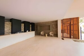 A modern interior with a stone wall, a reception desk, two chairs, and a wooden partition. - Edificio Martinique  (Cartagena)