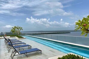 A rooftop pool with lounge chairs, a clear view of the sea, and a distant cityscape. - Edificio Martinique  (Cartagena)