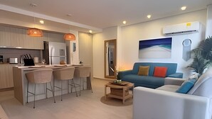 A modern kitchen with a bar area, a living room with a sofa and a painting, and a dining area with chairs. - Edificio Martinique  (Cartagena)