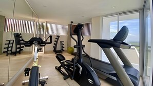 A gym with exercise equipment, a treadmill, and a large window with a view. - Edificio Martinique  (Cartagena)