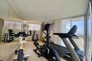 A gym with exercise equipment, a treadmill, and a large window with a view. - Edificio Martinique  (Cartagena)