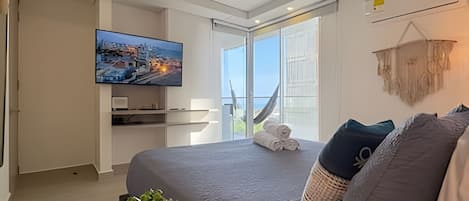 Une chambre moderne avec un grand lit, un téléviseur fixé au mur et une vue sur l’extérieur grâce à une porte coulissante.