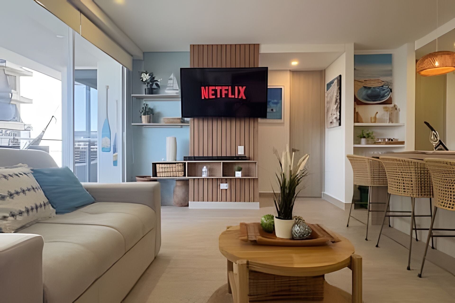 Una sala de estar moderna con un televisor de pantalla plana montado en la pared, un sofá, una mesa de centro y un comedor con sillas.