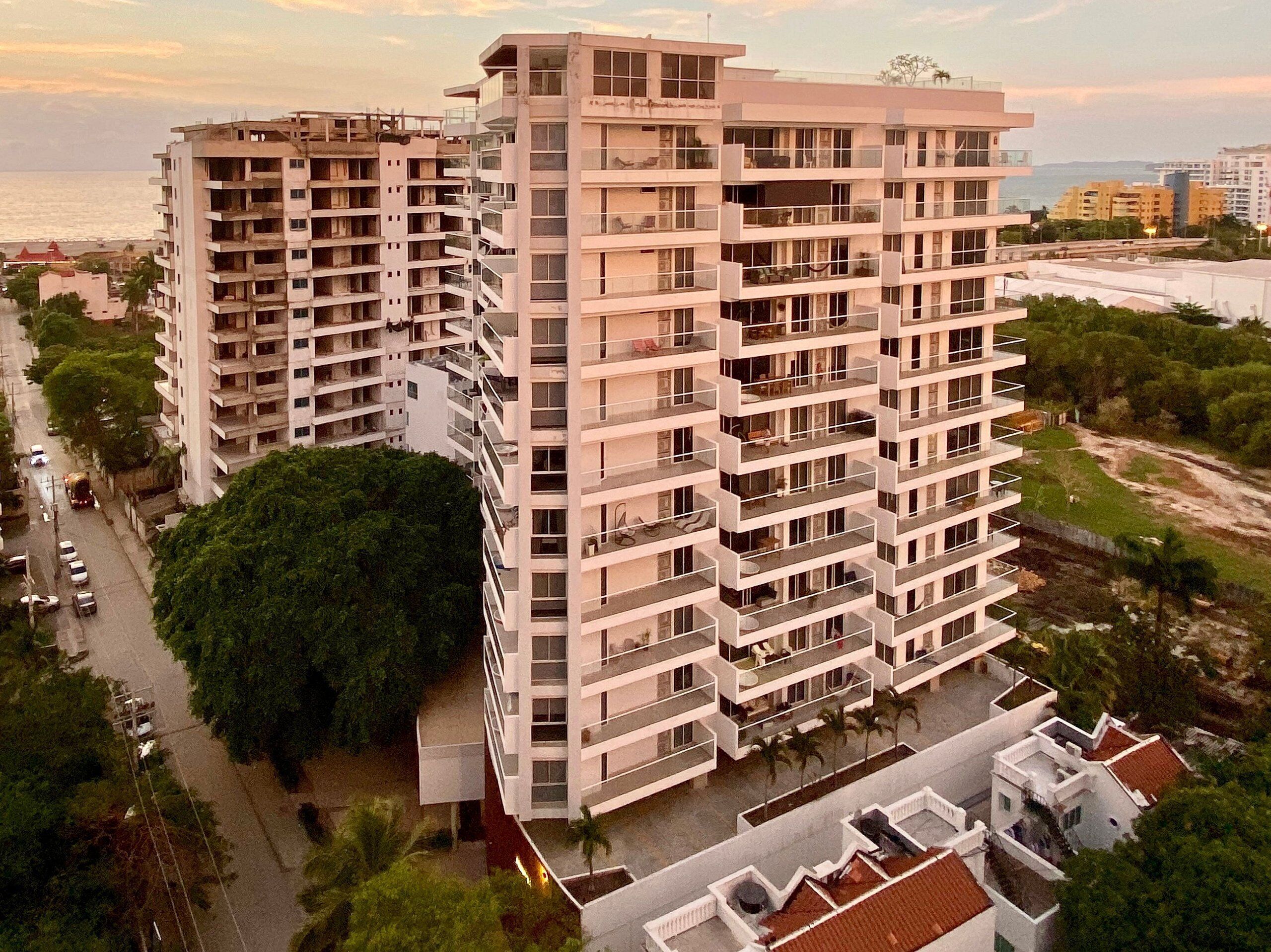 A multi-story residential building with balconies, a street view, and a body of water in the background.