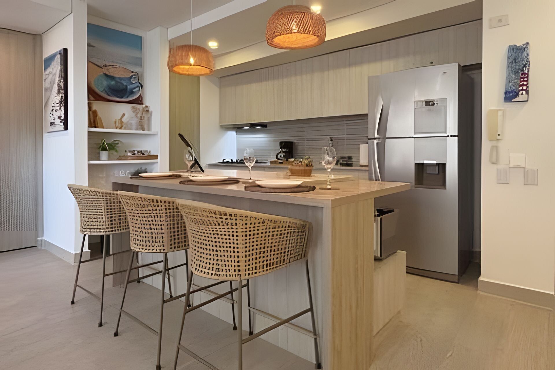 Una cocina moderna con una isla central, taburetes de bar, iluminación colgante y electrodomésticos de acero inoxidable.