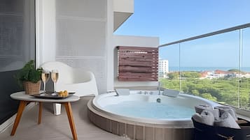Un balcón moderno con un jacuzzi, una mesa con vasos y pasteles, y vistas a la ciudad.