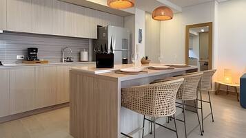 Una cocina moderna con una isla central, taburetes de bar, iluminación colgante y un comedor con mesa y sillas.