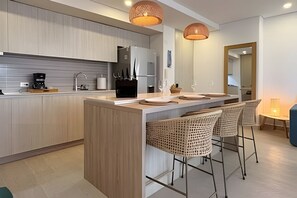 Una cucina moderna con isola centrale, sgabelli da bar, luci a sospensione e zona pranzo con tavolo e sedie.