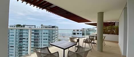 Un balcón moderno con una mesa y sillas, vistas a edificios altos y una estructura de techo de madera.