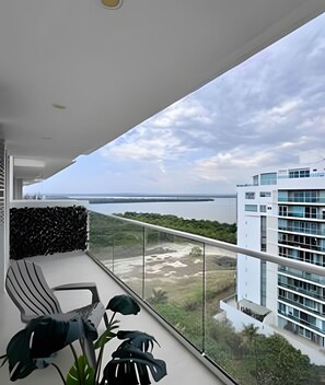Ein Balkon mit Blick auf ein Gewässer und eine entfernte Brücke, ein modernes Gebäude mit großen Fenstern und einem Blumentopf.