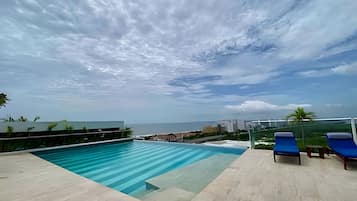 Una piscina con vistas al mar, un área de descanso con sillones y un cielo despejado.