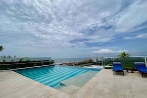 A swimming pool with a view of the sea, a lounge area with chairs, and a clear sky. - Edificio Martinique  (Cartagena)