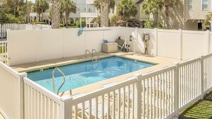 A rectangular swimming pool with a white fence, surrounded by a white wall and palm trees.