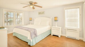 A bedroom with a bed, nightstands, a ceiling fan, and windows with blinds.