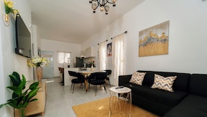 Een moderne woonkamer met een zwarte bank, een bijzettafeltje en een eethoek met tafel en stoelen.