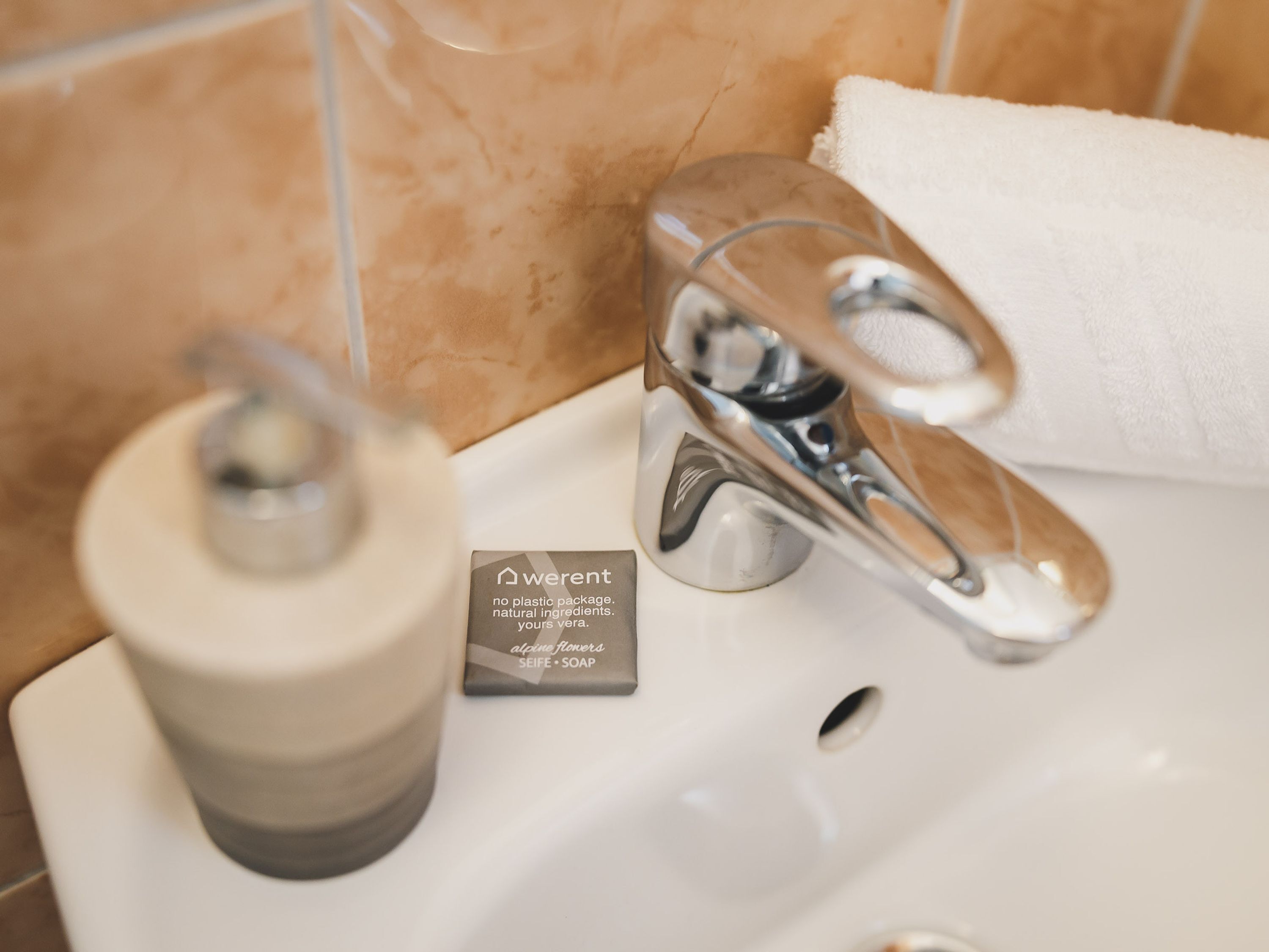 A bathroom sink with a white basin, a chrome faucet, and a soap dispenser. A sign next to the soap dispenser reads "weren't no plastic package, natural ingredients, yours vera."